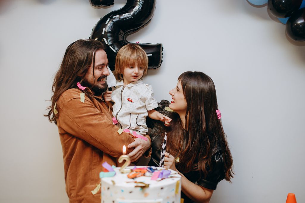 Happy family with child celebrating second birthday with cake and decorations indoors.